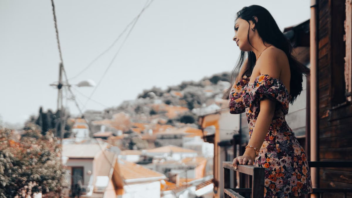 A fashionable woman in a floral dress stands on a balcony, overlooking the scenic cityscape of Istanbul.